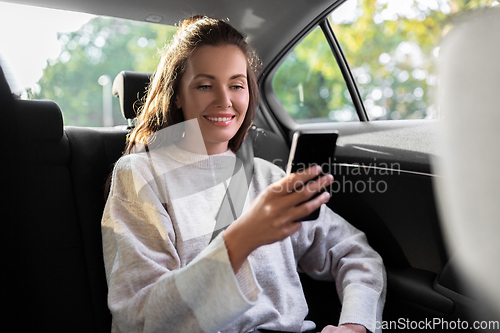 Image of smiling woman using smartphone in taxi car