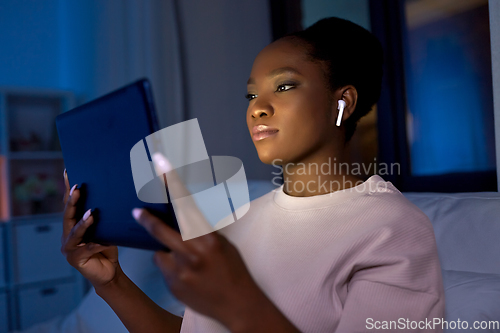 Image of woman with tablet pc in earphones in bed at night