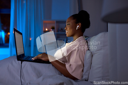 Image of woman with laptop and earphones in bed at night