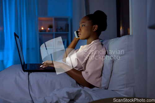 Image of woman with laptop calling on phone in bed at night