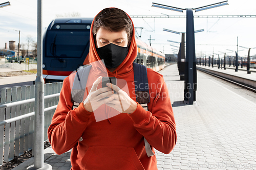 Image of man in mask with smartphone traveling by train