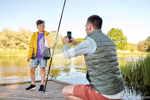 Image of father photographing son with fishing rod on river