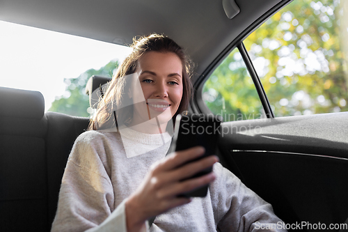 Image of smiling woman using smartphone in taxi car