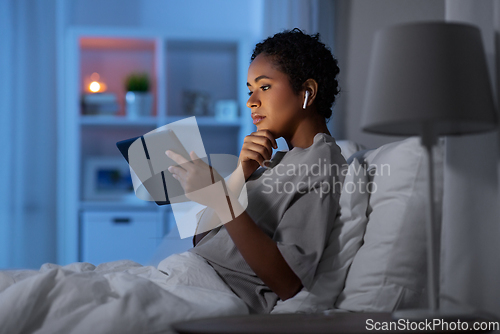 Image of woman with tablet pc in earphones in bed at night