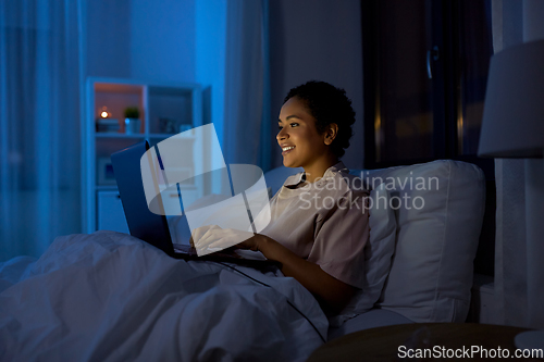 Image of woman with laptop in bed at home at night