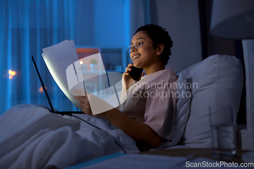 Image of woman with papers calling on phone in bed at night