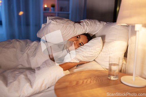 Image of angry african woman lying in bed and closing ears