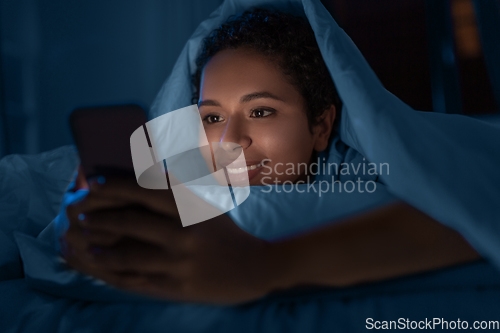 Image of woman with smartphone under duvet in bed at night