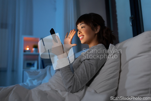 Image of woman with phone having video call in bed at night