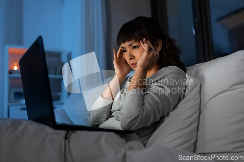 Image of stressed woman with laptop working in bed at night