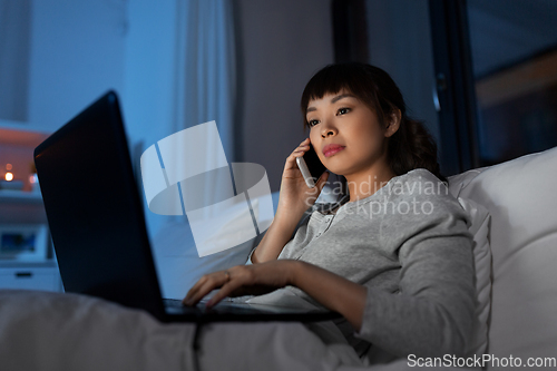 Image of woman with laptop calling on phone in bed at night