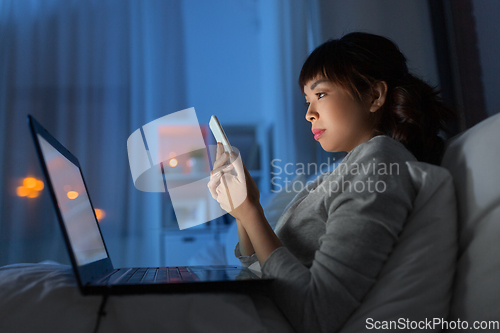 Image of asian woman with smartphone in bed at night