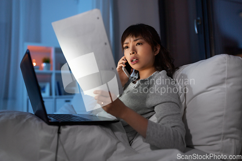 Image of woman with laptop calling on phone in bed at night
