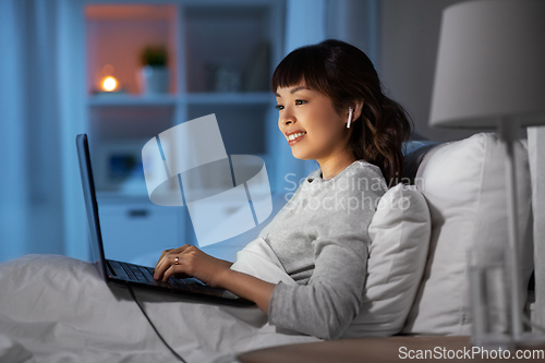 Image of woman with laptop and earphones in bed at night