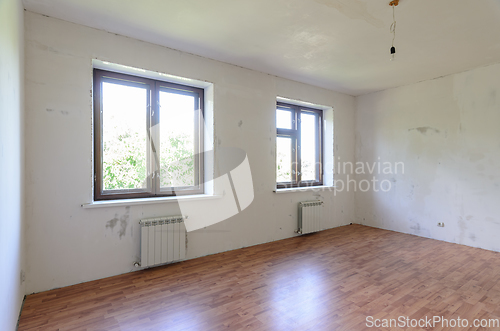 Image of The interior of an empty room during renovation, there are two large windows in the room, radiators under them