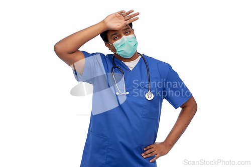 Image of tired indian male doctor in blue uniform and mask