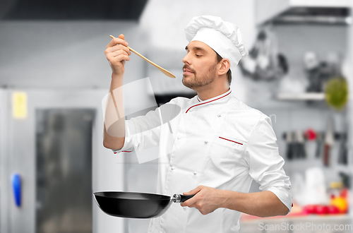 Image of happy male chef with frying pan tasting food