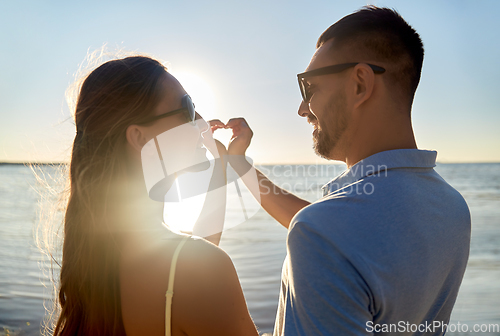 Image of happy couple showing hand heart on summer beach