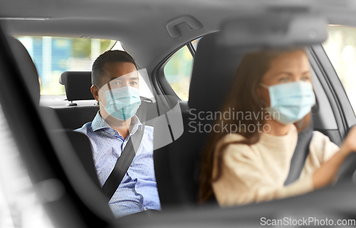 Image of female driver in mask driving car with passenger