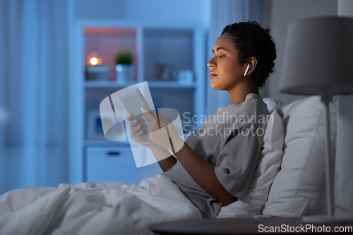 Image of woman with tablet pc in earphones in bed at night