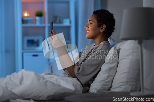 Image of african woman with smartphone in bed at night