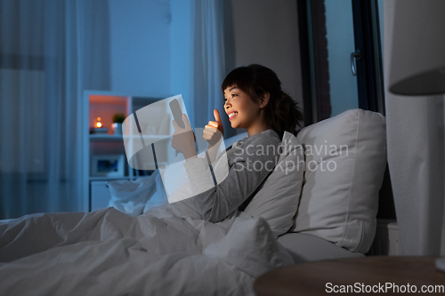 Image of woman with phone having video call in bed at night