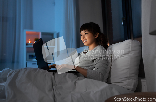 Image of woman with laptop in bed at home at night