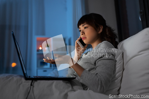 Image of woman with laptop calling on phone in bed at night