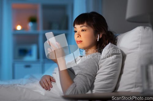 Image of woman with phone and earphones in bed at night