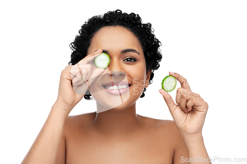 Image of happy african woman making eye mask of cucumbers