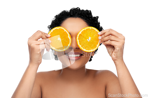 Image of smiling african woman making eye mask of oranges