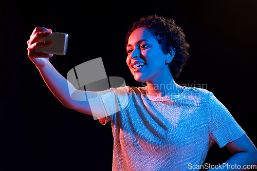 Image of woman taking selfie with smartphone in neon lights