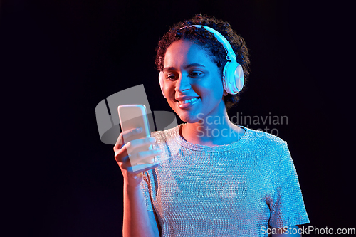 Image of woman in headphones with smartphone in neon lights