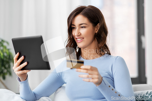 Image of happy woman with tablet pc and credit card at home