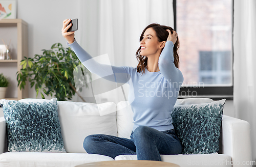 Image of happy woman with smartphone taking selfie at home