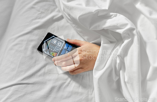 Image of hand in bed with smart home icons on smartphone