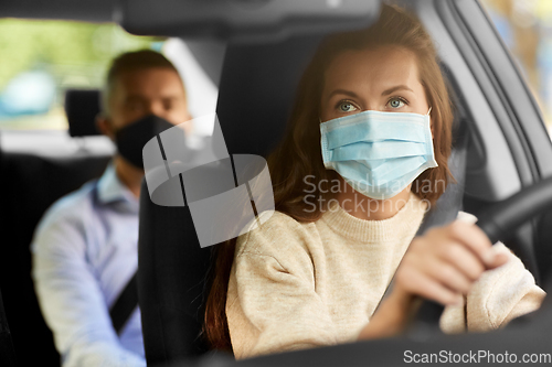 Image of female driver in mask driving car with passenger