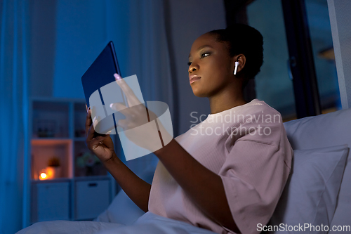 Image of woman with tablet pc in earphones in bed at night