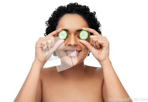 Image of happy african woman making eye mask of cucumbers