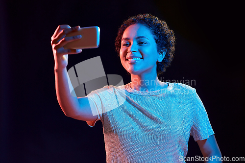 Image of woman taking selfie with smartphone in neon lights