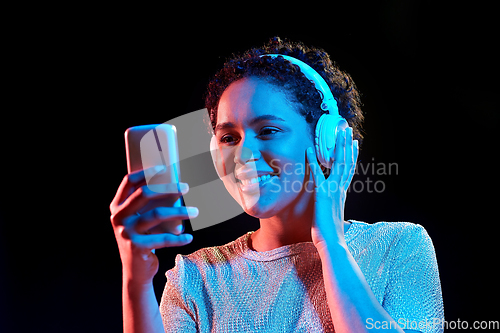 Image of woman in headphones with smartphone in neon lights