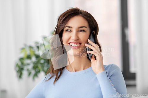 Image of smiling woman calling on smartphone at home