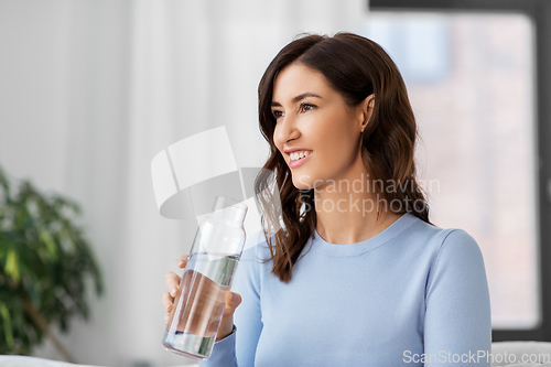 Image of woman drinking water from glass bottle at home