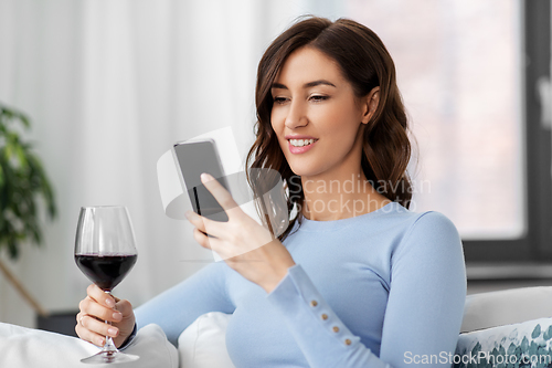 Image of woman with smartphone drinking red wine at home