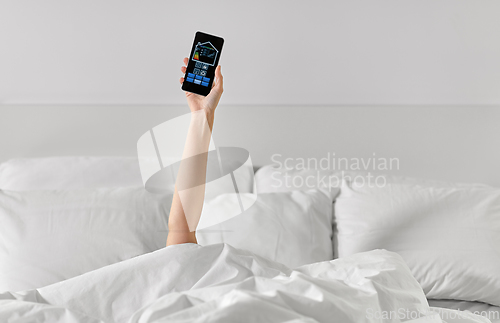 Image of hand in bed with smart home icons on smartphone