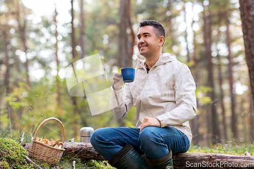 Image of man with basket of mushrooms drinks tea in forest