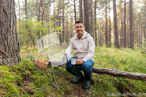 Image of man with basket of mushrooms drinks tea in forest