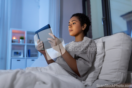 Image of woman with tablet pc in bed at home at night