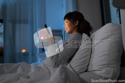 Image of asian woman with smartphone in bed at night
