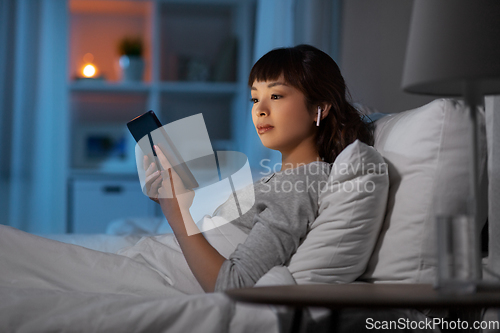 Image of woman with tablet pc in earphones in bed at night